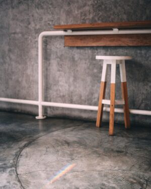 Solid oak counter stool against a concrete wall
